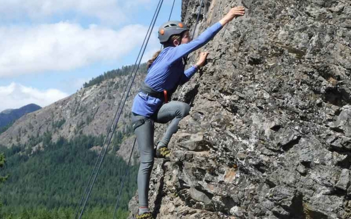 a student scales a rock wall on an outward bound trip for teens